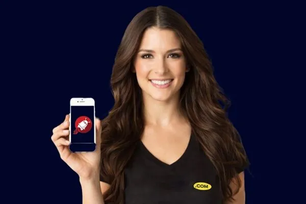 A smiling woman holds a smartphone displaying a logo, wearing a black shirt with a yellow dot com emblem against a dark background.