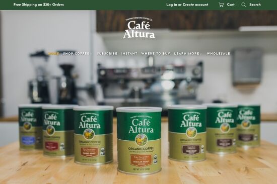 Several cans of Café Altura coffee displayed on a wooden surface, with a background featuring coffee machines and a cozy café ambiance.