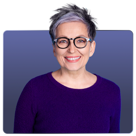 A smiling woman with short, stylish gray hair and glasses, wearing a purple sweater, against a gradient blue background.