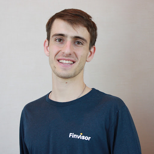 A young man with short hair smiles, wearing a navy blue long-sleeve shirt featuring the logo of "FinVisor." The background is a light, neutral color.